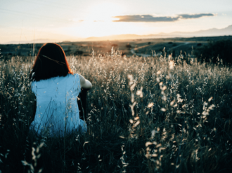 Kvinna som kollar ut över ett fält vid solnedgång