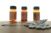 Piller utspridda på ett bord, 3 suddiga medicinburkar i bakgrunden
