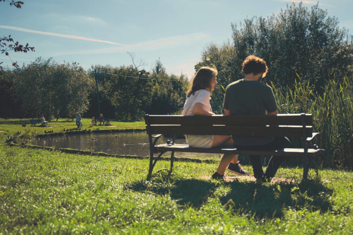 Man och kvinna sitter i solljus på en bänk omgiven av grönska