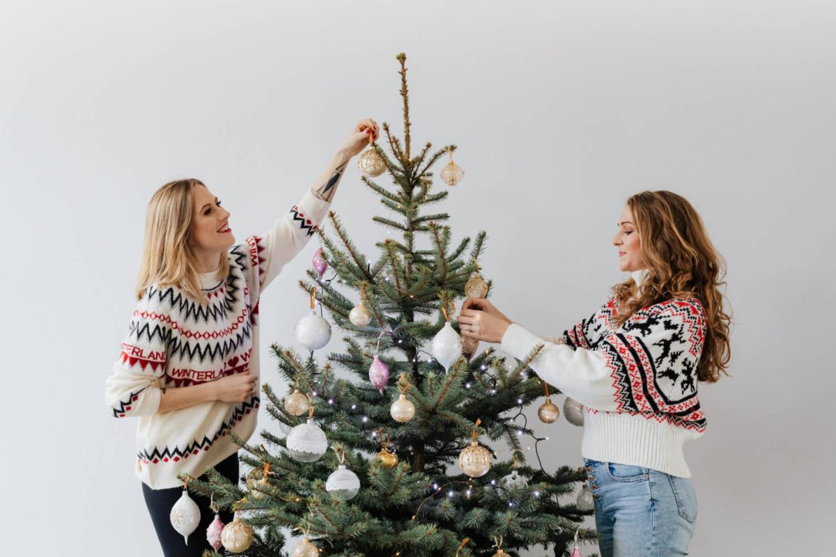 Två kvinnor jultröjor klär en julgran