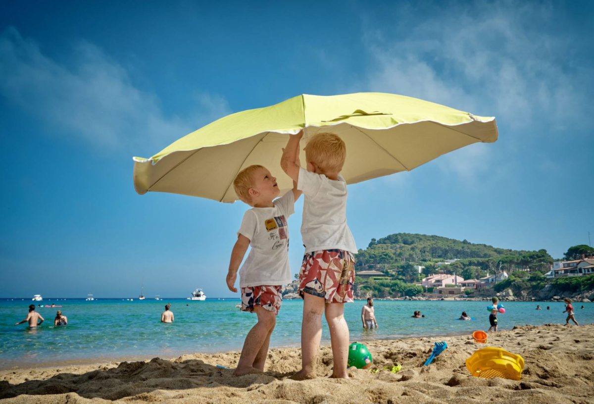 Två barn på stranden i skydd av parasoll