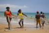 Många bybor hjälper till att dra upp ett nät på stranden