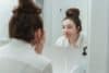 Kvinna som står framför spegeln och inspekterar sin hy